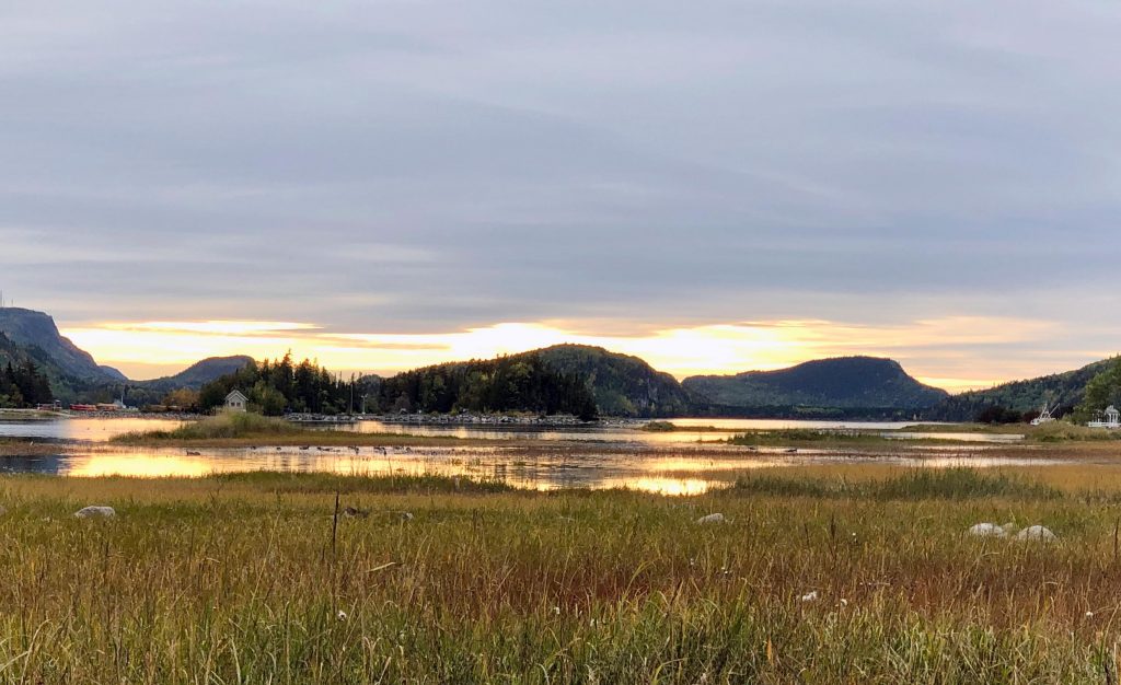Landscape. Foreground with marshy grass then water. Small mountains in the background. Sunset on the south shore of the St-Laurence River.