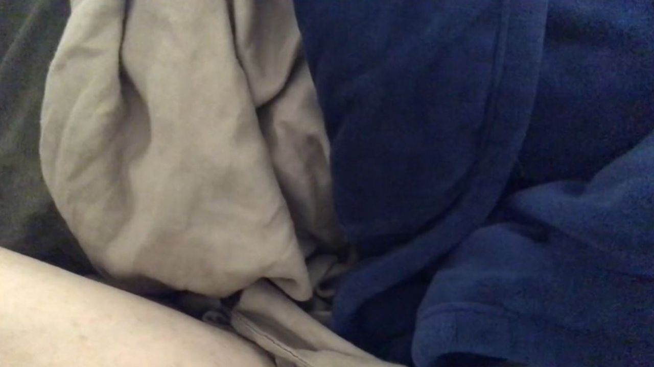 Partial close up of human forearm covered by a beige bed sheet and soft blue blanket. 