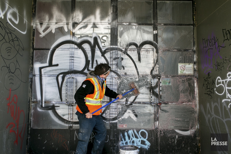 Man wearing orange security vest scrubs a garage door in an alcove of graffiti.
