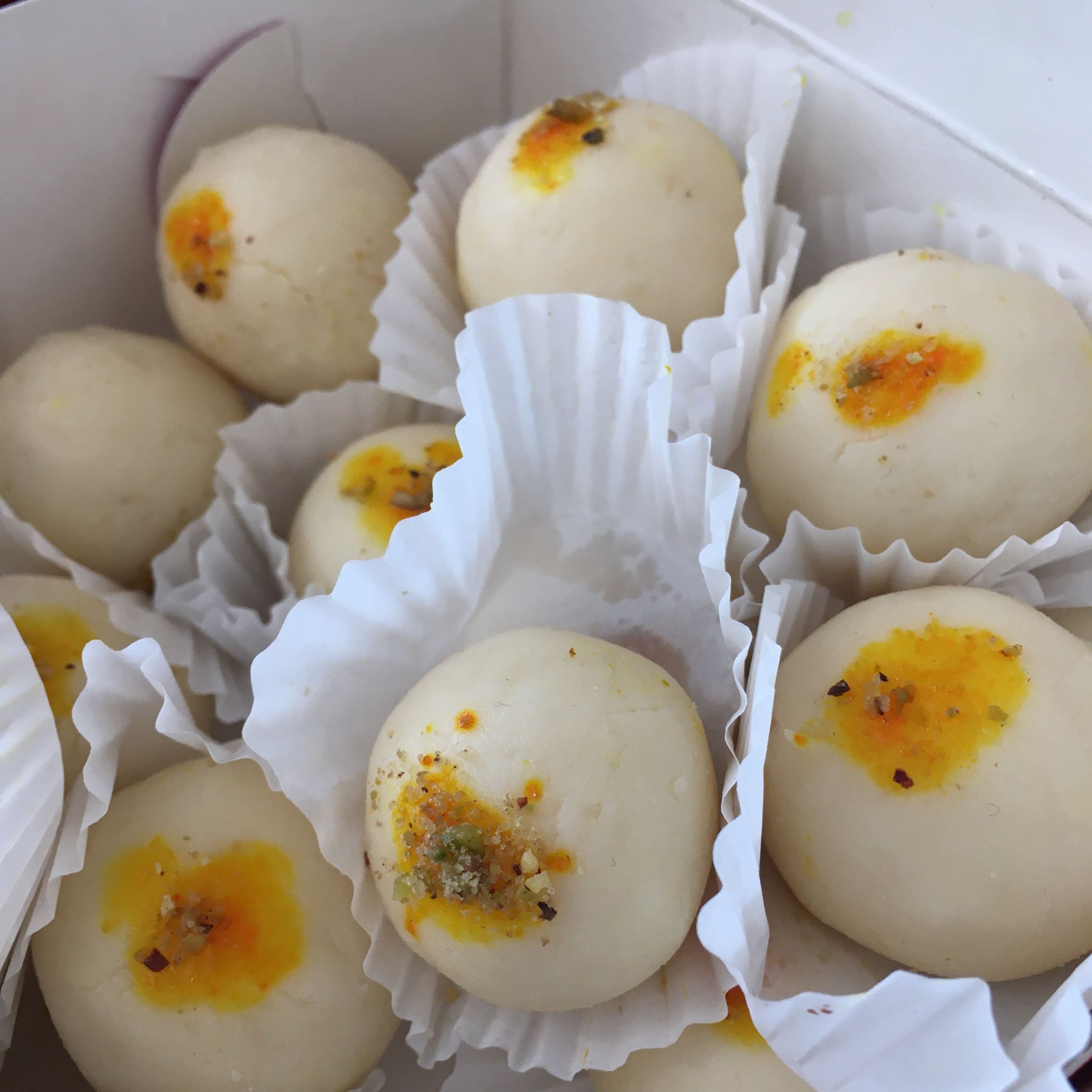 A box of many round sweets sprinkled with pistachio and amber; each one in a muffin wrapper. 